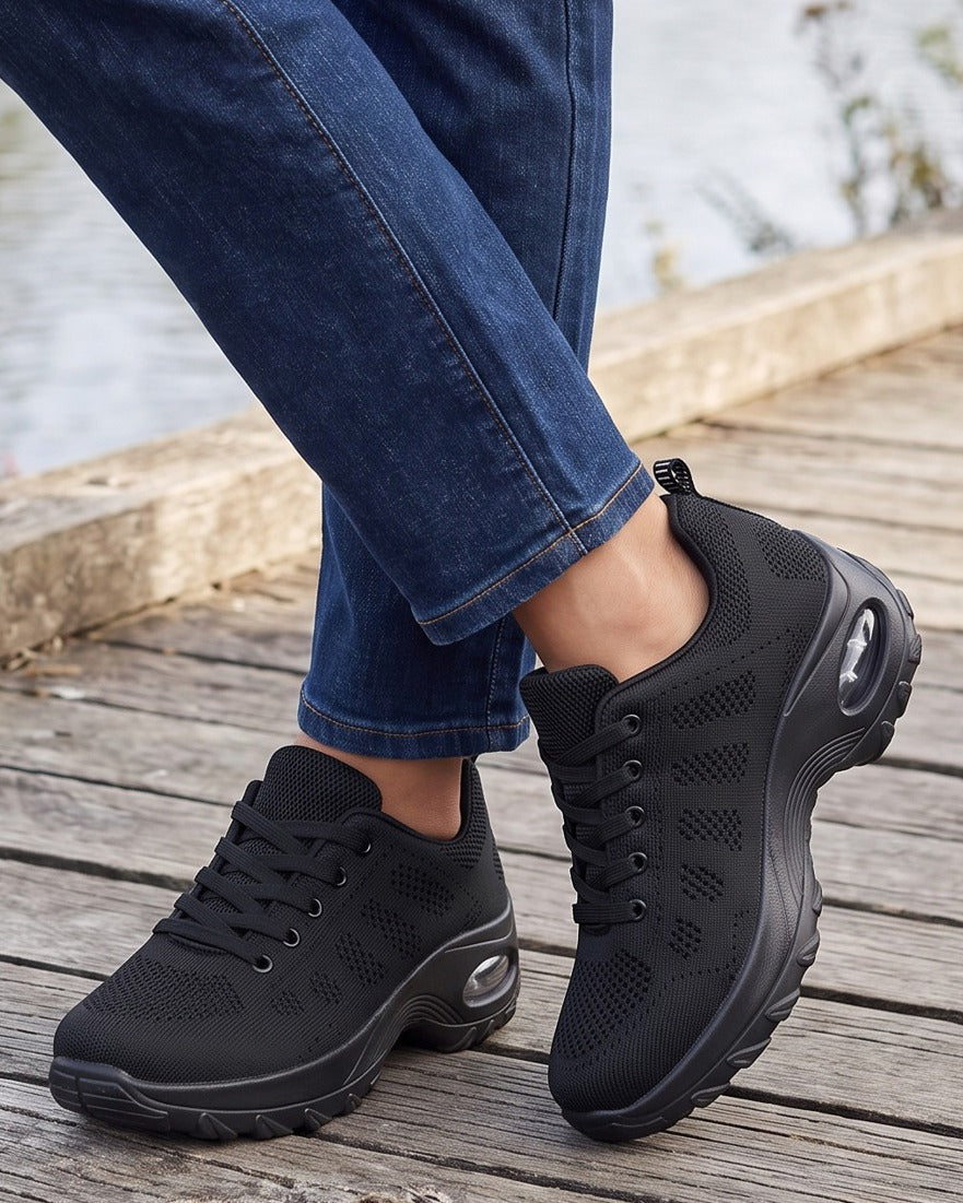 Nell black sneakers worn with jeans on a riverside boardwalk