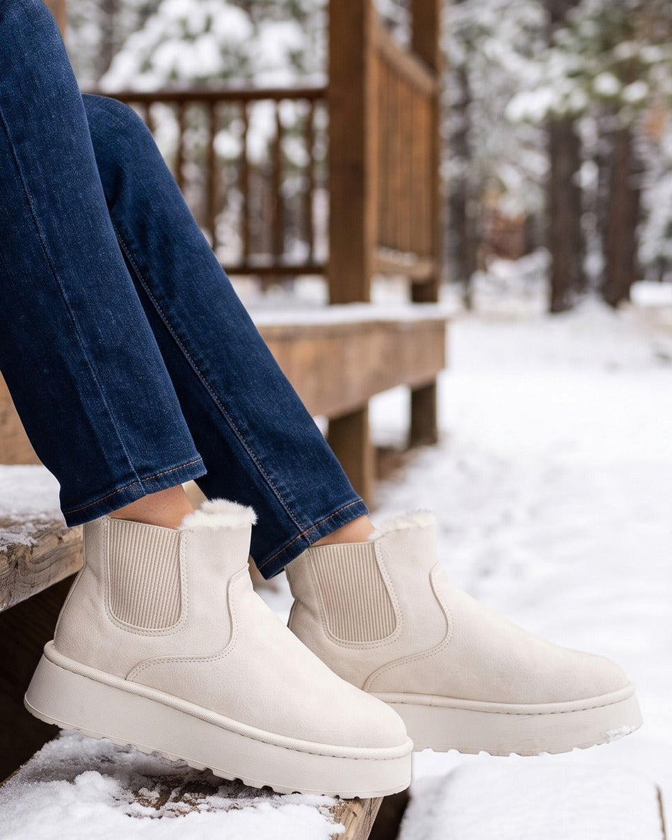 Coral cream snow boots worn with jeans, seated on snowy cabin steps