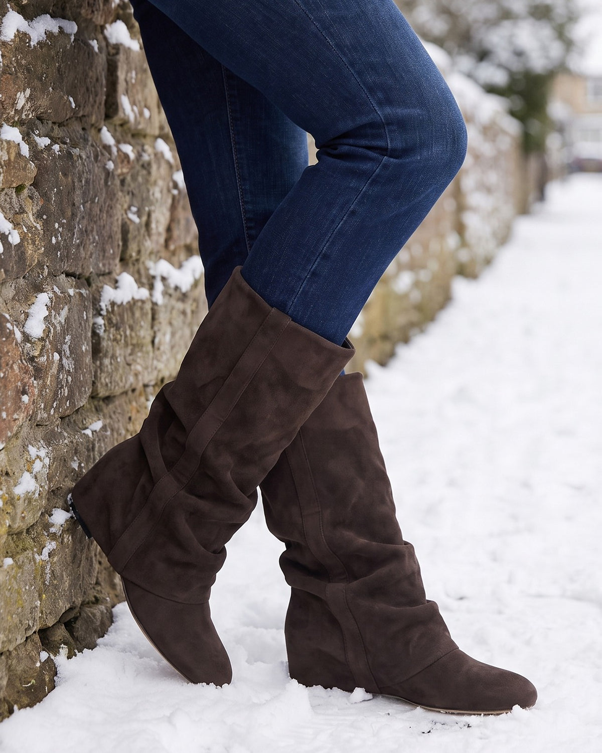 Hattie slouch boots worn with jeans on a snowy path by a stone wall