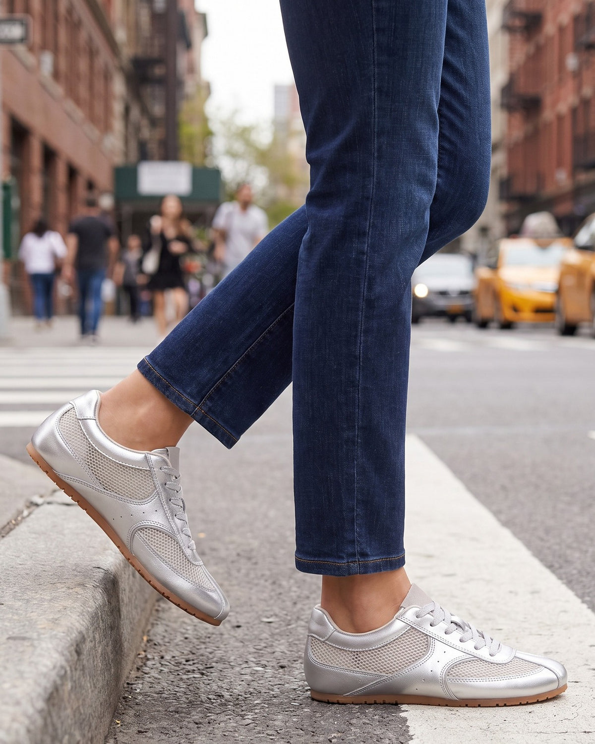 Juno silver sneakers worn with jeans, stepping off a city curb