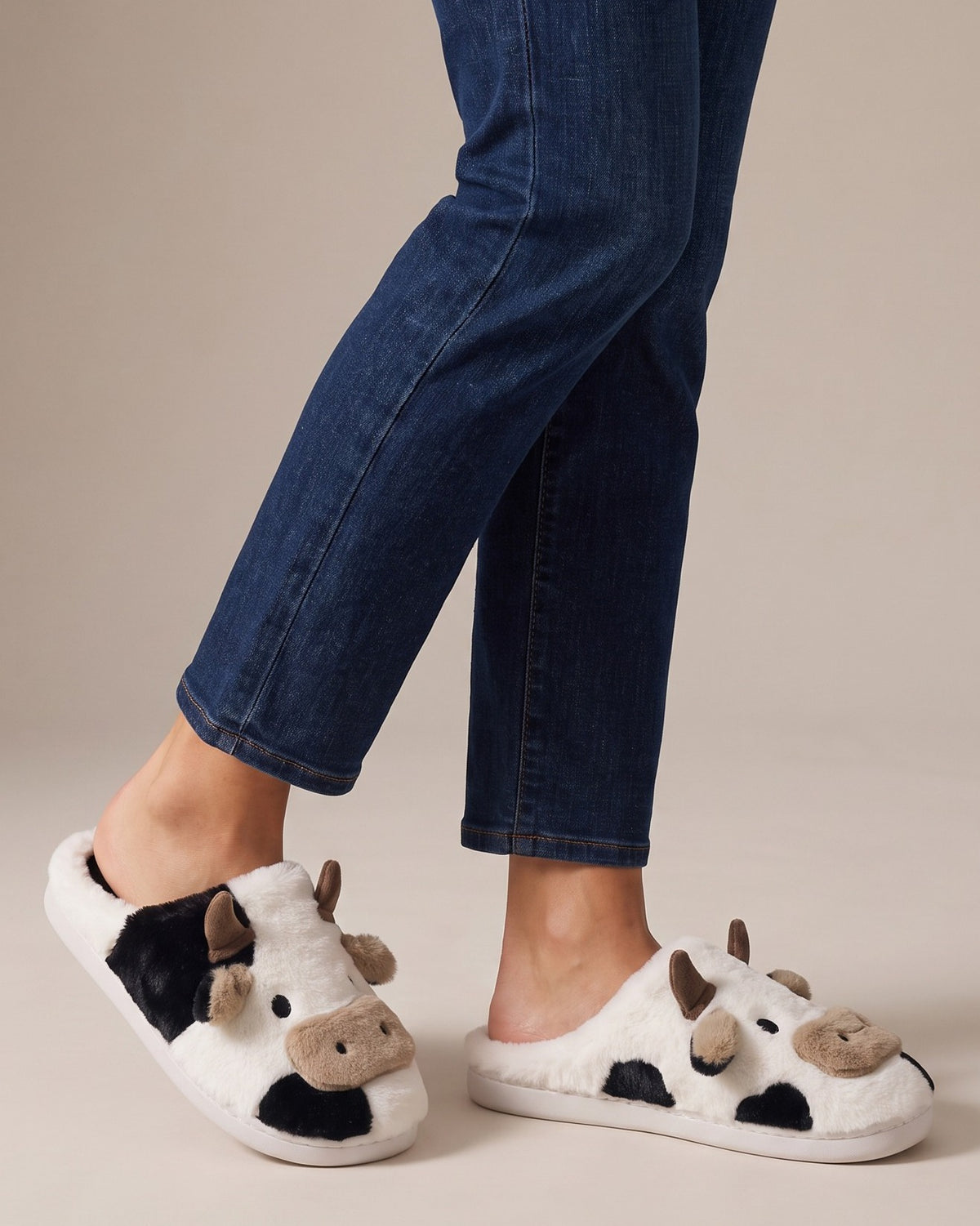 Odette cow-print slippers worn with jeans, studio shot of legs