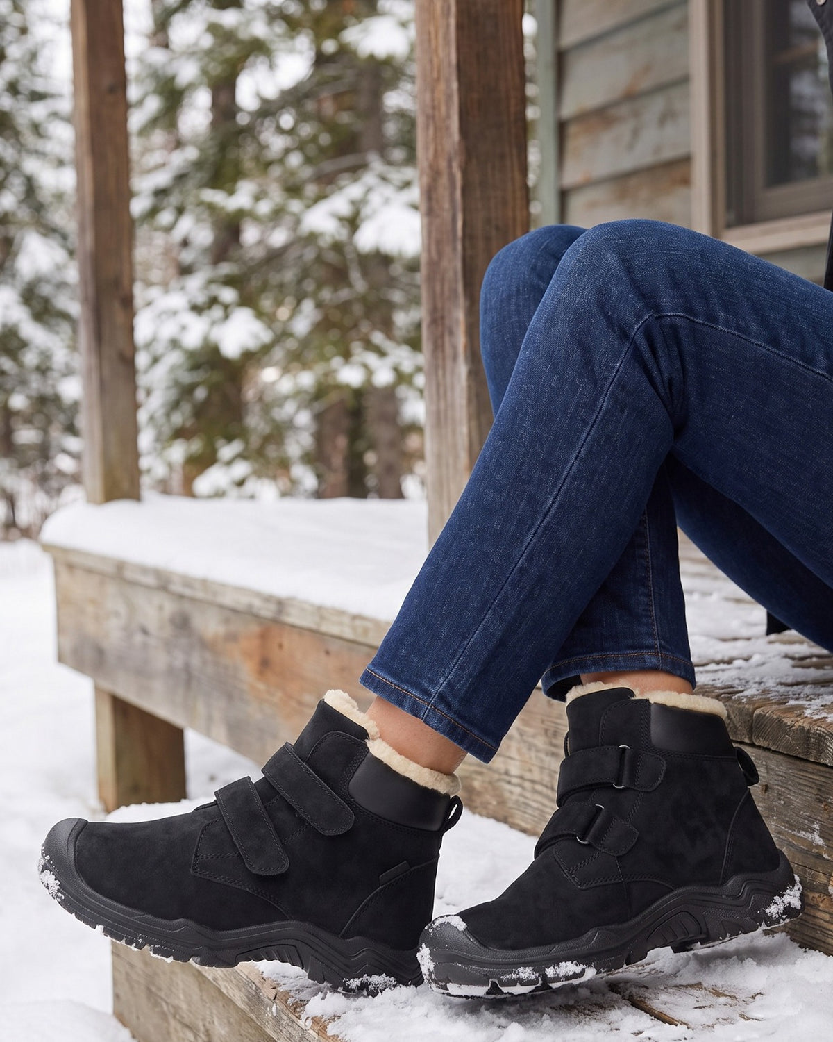 Rosa black ankle boots worn with jeans, seated on snowy wooden steps