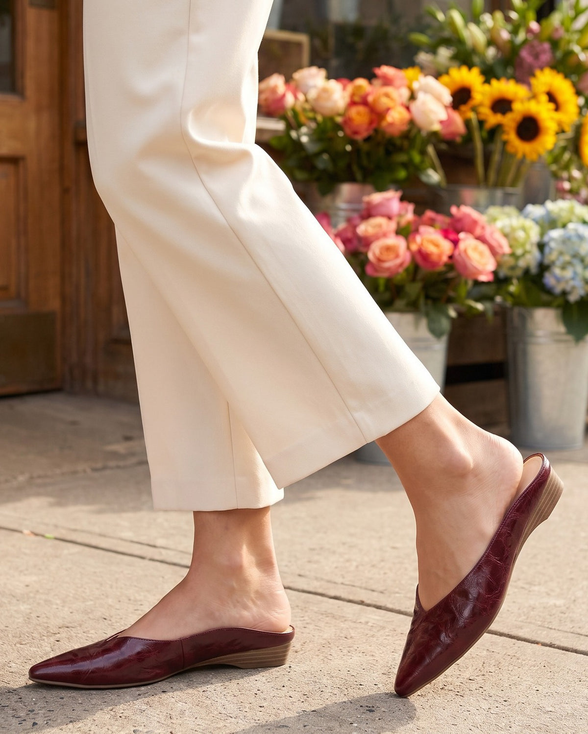 Thea burgundy mules worn with cream trousers outside a flower shop